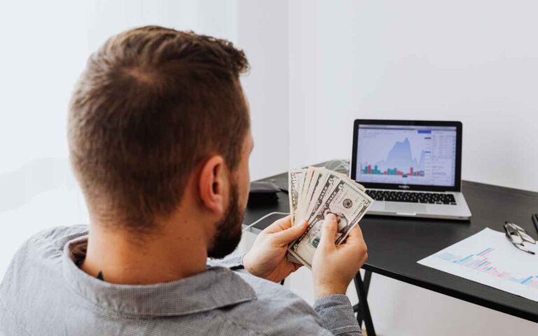 Man with money on his hand while on a laptop